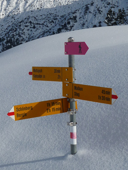 fast eingeschneiten Wegweiser mit einem Hinweisschild für den Winterwanderweg oben